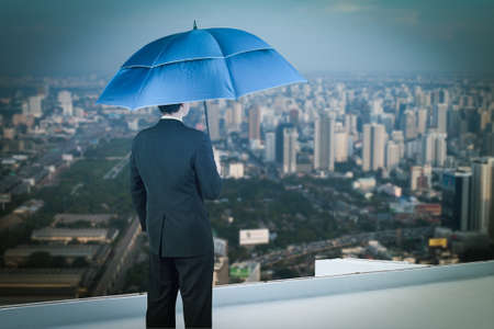 Back view of businessman with umbrella on the rooftop and looking at cityの写真素材