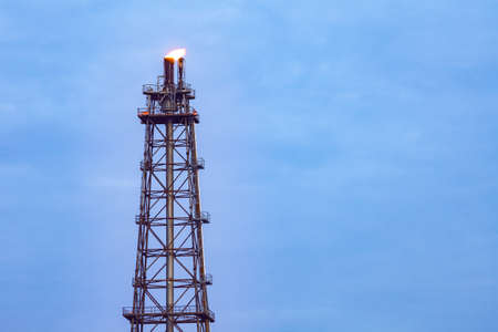 Tower chimney of Oil refinery with fire on top on blue cloud sky background, business industry factory conceptの写真素材