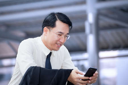 businessman sitting and using a cell phone with modern office building backgroundの写真素材