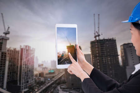 Asian business engineer architecture professional woman, wearing safety helmet and use smartphone to capture construction site for working and presenting job conceptの写真素材