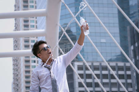 Asian Businessman standing and happy to drink water and hold bottle and modern city backgroundの写真素材
