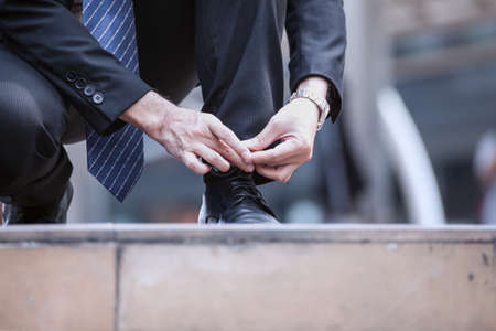 Businessman tie shoelace or lace up black shoes on floor, close upの写真素材