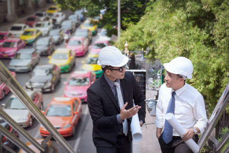 Asian businessman discuss with engineer architect professional wearing safety helmet and holding construction plan roll in hand for working team together conceptの写真素材