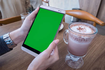 woman hand holding mobile phone with green screen for advertising text message or promotional content, reading news on cell telephone in coffee placeの写真素材