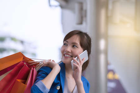 asian woman shopping smile and holding  shopping bag with cell phone, consumerism, sale and people online conceptの写真素材