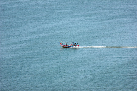 A small, colorful fishing boat with several people on board moves swiftly across the calm,...