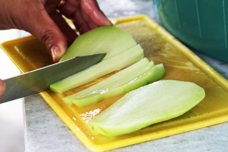 Cutting Melon on a yellow cutting board with a knife.の写真素材