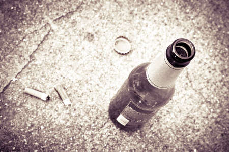 Bottle of beer resting on the ground with three cigarette's butts.Alcoholism and tobacco addiction concept - toned imageの写真素材