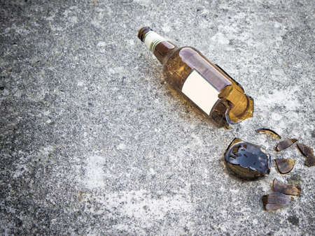Shattered brown beer bottle resting on the ground: alcoholism concept - toned imageの写真素材