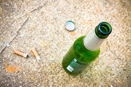 Bottle of beer resting on the ground with three cigarette's butts.Alcoholism and tobacco addiction...