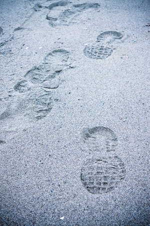 Heavy footprint left on a muddy sand by a male boot. Little vignette effect added - toned imageの写真素材
