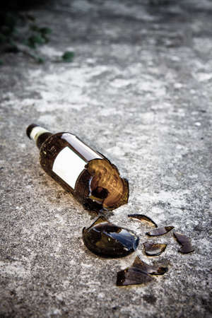 Shattered brown beer bottle resting on the ground: alcoholism concept - toned imageの写真素材