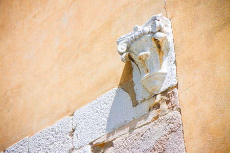 Corinthian capital in stone and plaster wall (Italy)