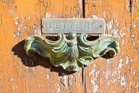 Old postal brass mailbox gainst a colored wooden doorの写真素材