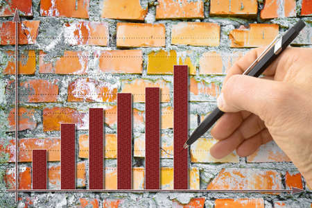 Hand draws a growing graph against a brick wall background - concept imageの写真素材