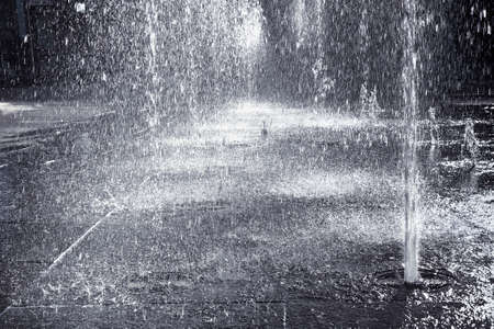 Water jets of a modern fountain on a stone pavement - toned imageの写真素材