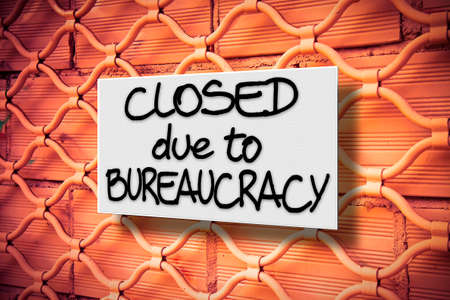 Closed due to bureaucracy - concept image with a warning sign against a closed metal shutterの写真素材