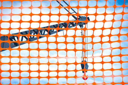 Construction site with safety plastic orange grid against a tower crane.