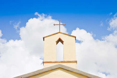 Old italian little church with metal Christian cross on the top against a cloudy sky - concept image with copy space.の写真素材