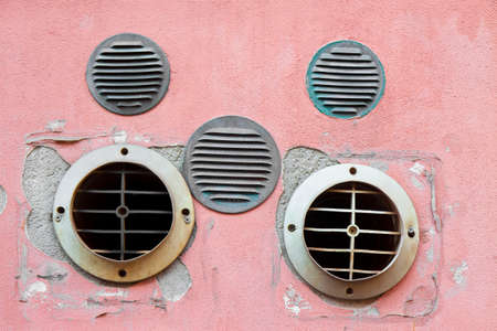 Copper and plastic ventilation grilles against an old and damaged plaster wall.