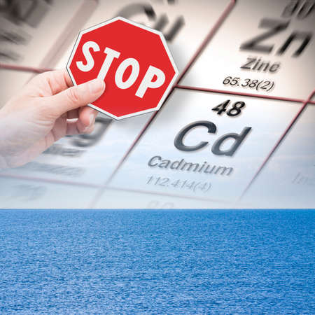 Stop pollution from dangerous cadmium and heavy metals in seawater - concept with hand holding a stop sign against a cadmium chemical element with the Mendeleev periodic table on seawater background.の写真素材
