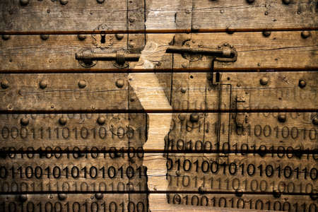 Violation of the secret code file - concept image with binary code agaist an old rusty metal door on wooden backgroundの写真素材