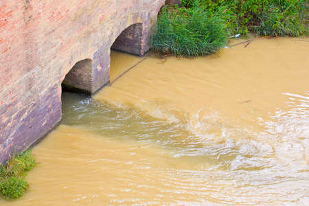 Dangerous, untreated, toxic polluted water flows from a city sewer to the river.の写真素材