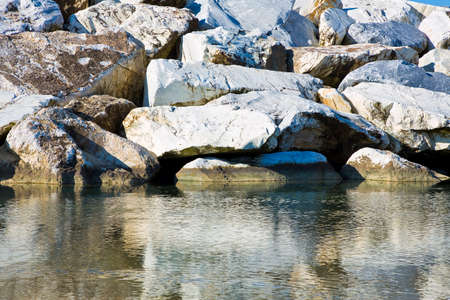 Stone breakwater rocks are reflected in the water.の写真素材