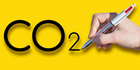 Female hand writing CO2 text over a solid colored background.