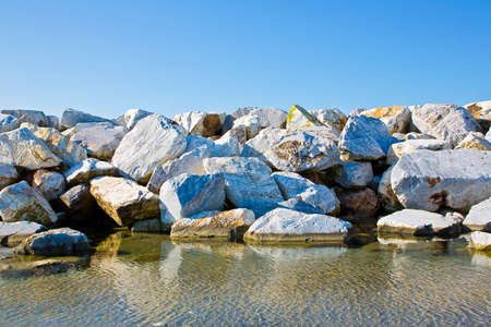 Stone breakwater rocks are reflected in the water - image with copy space on sky.の写真素材