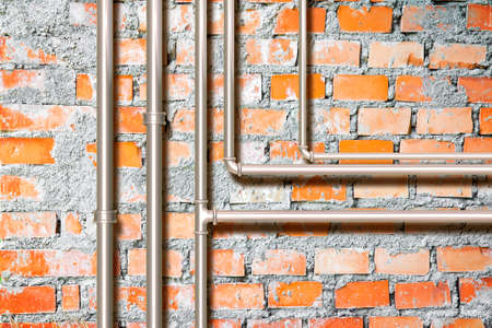 Water and gas pipeline in front of an old brick wallの写真素材