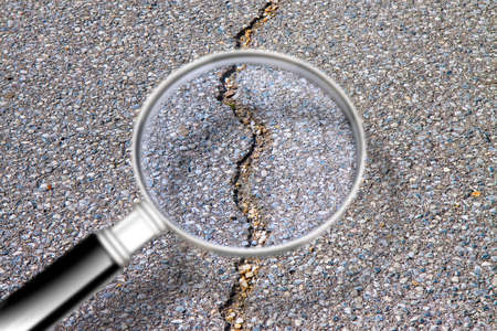 Cracked asphalt road damaged after a structural failure - Concept image seen through a magnifying glassの写真素材