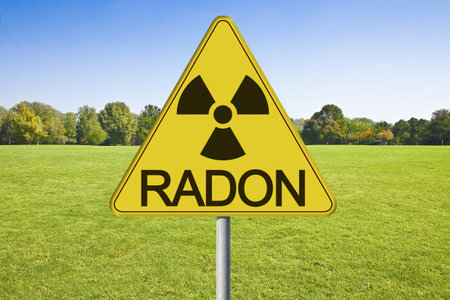 Danger of radioactive contamination from RADON GAS - concept with warning symbol of radioactivity on road sign against a building lot and vacant land available for building construction.の写真素材