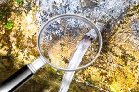Checking the water purity of public drinking fountains - Are drinking fountains safe and free from germs, bacteria and virus? - concept with water gushing seen from a magnifying glassの写真素材