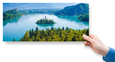 Bled lake, the most famous lake in Slovenia with the island of the church (Europe - Slovenia) - panoramic view - concept image with a female hand holding an postcard.の写真素材
