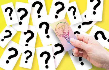 A female hand holding a card with a colored light bulb - solution concept against a background of...