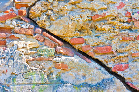 Deep crack in old brick and stone wall with damaged plasterの写真素材