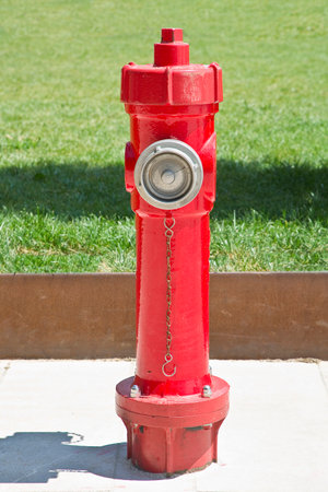 Metal fire hydrant colred in red with fresh green meadow in a public park