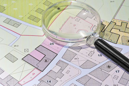 Imaginary cadastral map with buildings, land parcel and vacant plot - property registry and real estate concept seen through a magnifying glassの写真素材