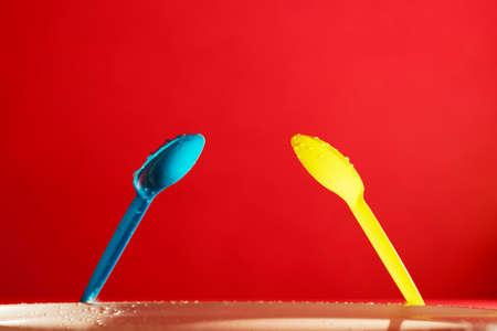 yellow and blue plastic spoonfuls on a red backgroundの写真素材