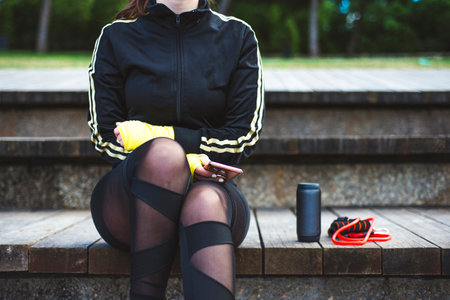 Portrait of a sporty young woman sit on wood stairs with phone.の写真素材