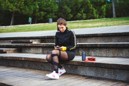 Portrait of a sporty young woman sit on wood stairs with phone.の写真素材