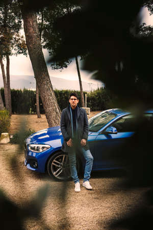 Young man sitting in front of his blue car while waitingの写真素材