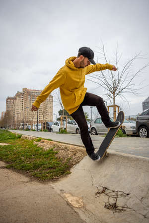Young caucasian male in a yellow hoodie and black cap jumping with his skateの写真素材
