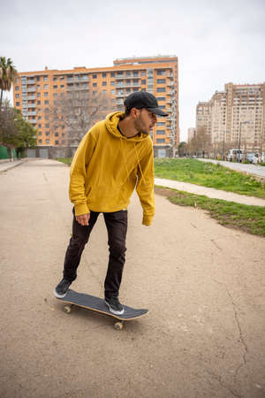 Young caucasian male in a yellow hoodie and black cap standing on his skateboard