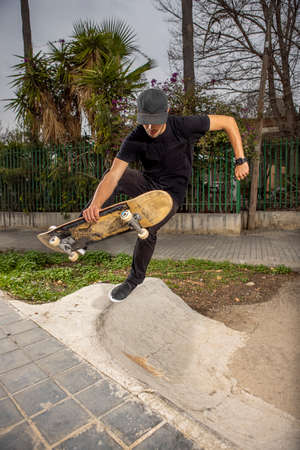 Young caucasian male in a black shirt and cap jumping with his skateboardの写真素材