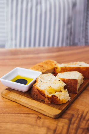 Vertical shot of slices of bread on a cutting board with a small bowl of oil next to themの写真素材