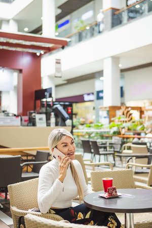 Vertical shot of a blonde Hispanic female talking on the phone in cafeの写真素材