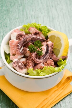 photo of delicious octopus salad appetizer on green glass table with yellow clothの写真素材