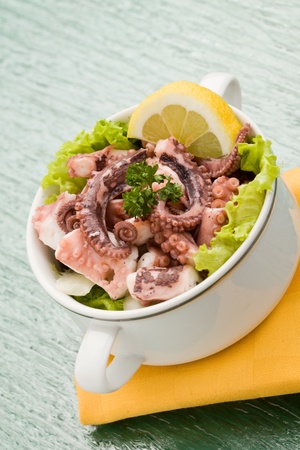 photo of delicious octopus salad appetizer on green glass table with yellow clothの写真素材
